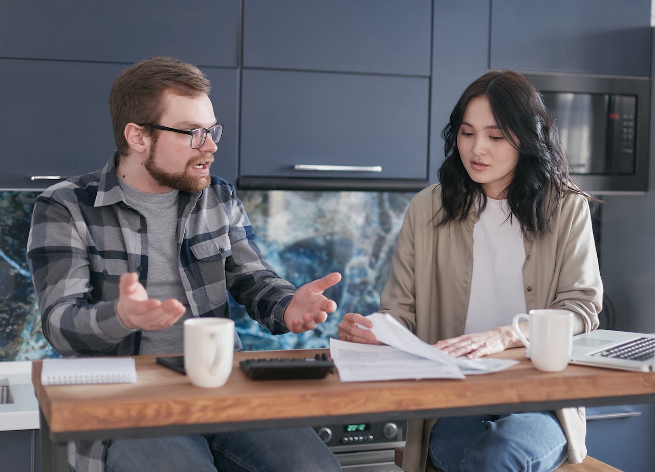 A man and woman discussing financial documents at a kitchen counter, looking concerned.